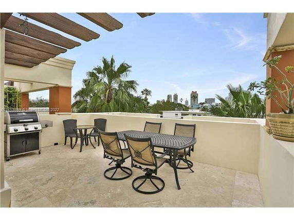 Rooftop patio with chairs, table, and a grill; view of palm trees and distant buildings.