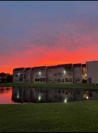 Front view of a multi-story building overlooking a small pond during sunset.