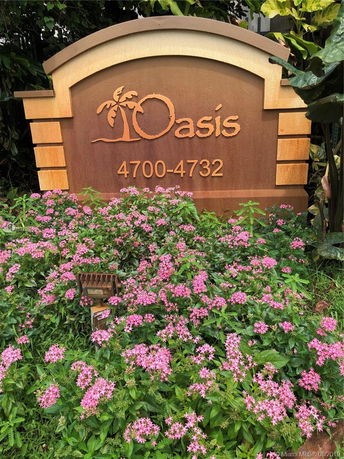 Hotel sign with 'Oasis 4700-4732' surrounded by pink flowers.