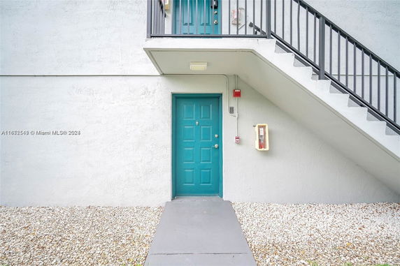 Front view of a building entrance with a teal door and exterior staircase.