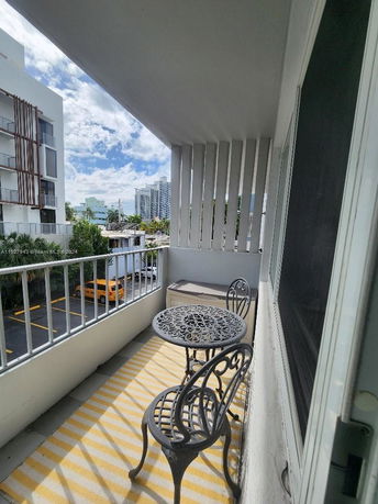Balcony view overlooking neighboring buildings and a parking area with a decorative metal table and chairs.