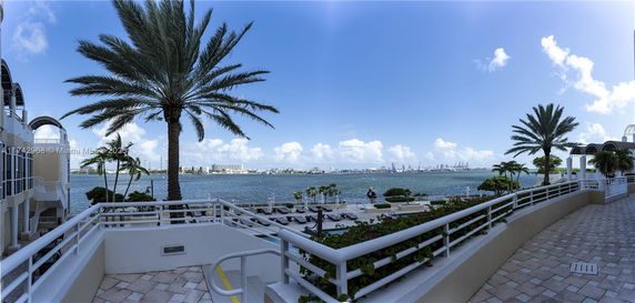 Panoramic view of waterfront area with palm trees and buildings in the background.