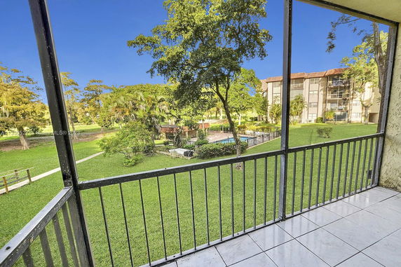 View of landscaped grounds with trees and a pool area from a balcony.