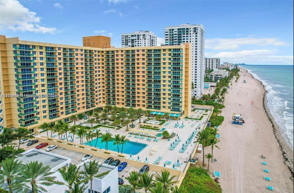 A large beachfront apartment building with multiple stories, featuring balconies and a spacious pool area.