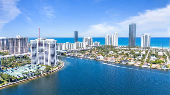Aerial view of tall buildings near a body of water with a coastline in the background.