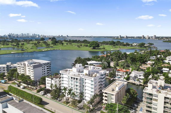 Panoramic view of residential area with buildings overlooking water and a golf course in the distance.