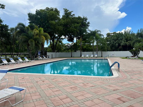 View of an outdoor swimming pool with surrounding lounge chairs and trees.