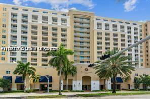 Front view of a multi-story apartment building with balconies and palm trees in front.