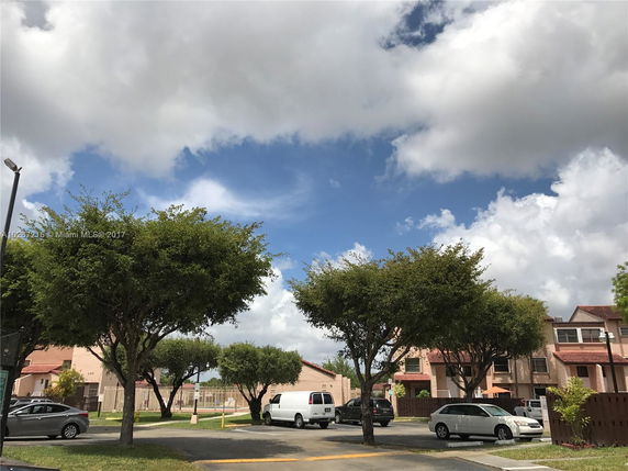 View of residential area with multiple townhouses and parked cars under a cloudy sky.
