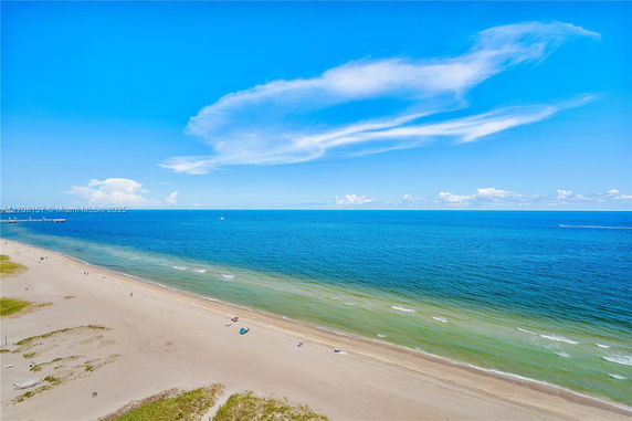 Panoramic view of a sandy beach and ocean under a clear blue sky.