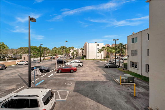 Outdoor parking area with multiple parked cars next to a multi-story building.