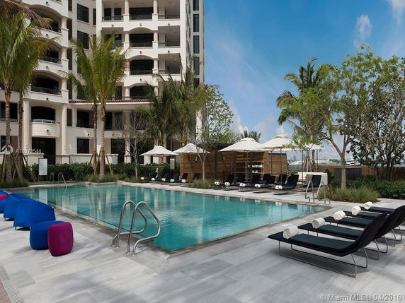 View of a multi-story building with balconies, adjacent to a pool area with lounge chairs and umbrellas.