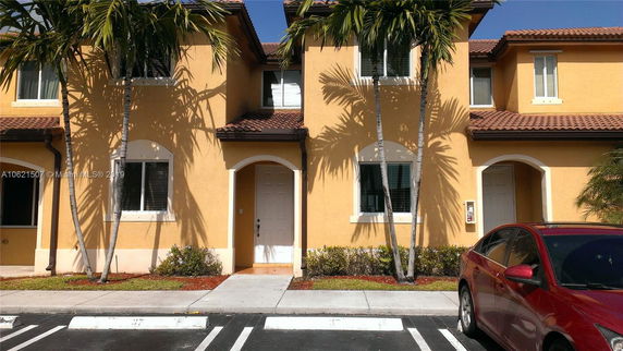 Front view of a two-story house with a tiled roof and an adjacent parking area.