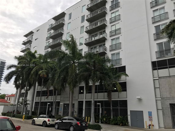 Front view of a multi-story residential building with balconies and palm trees.