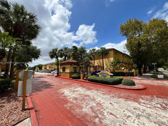 Front view of an apartment complex entrance with a yellow building and palm trees.