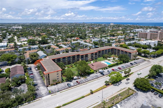 Aerial view of a residential area featuring a large U-shaped apartment building with a swimming pool, surrounded by roads and smaller houses.