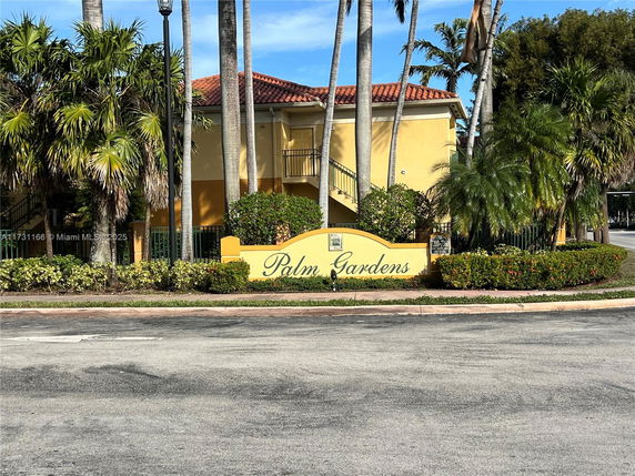Front view of a building with a yellow exterior and decorative palm trees, featuring a sign that reads 'Palm Gardens.'