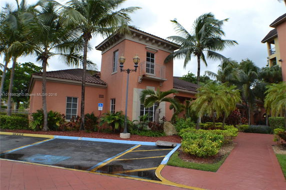 Front view of a two-story building with palm trees and a parking area.