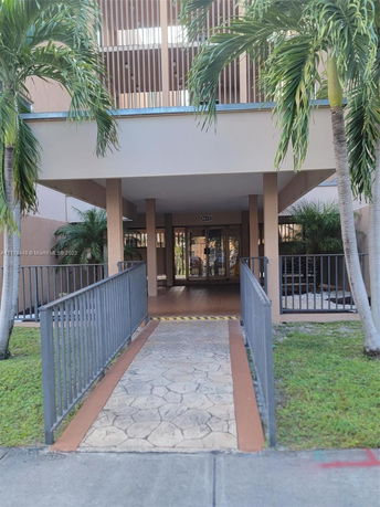 Entrance view of a multi-story building with a paved walkway and palm trees.