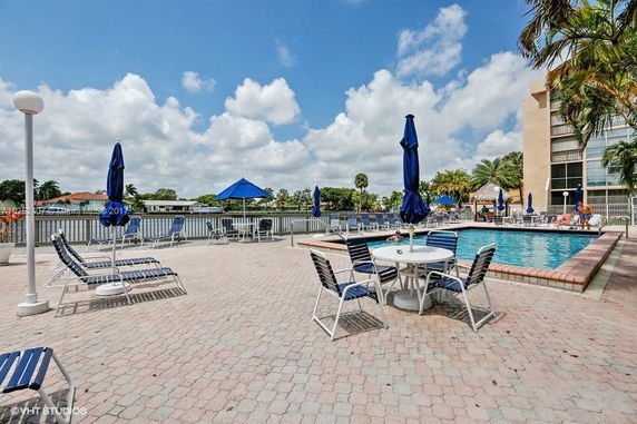 Outdoor area with a swimming pool surrounded by lounge chairs and tables with umbrellas.