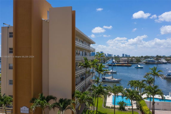 Side view of a multi-story building with balconies overlooking a waterfront with boats.