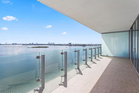View from a balcony with glass railing overlooking a body of water and distant city skyline.