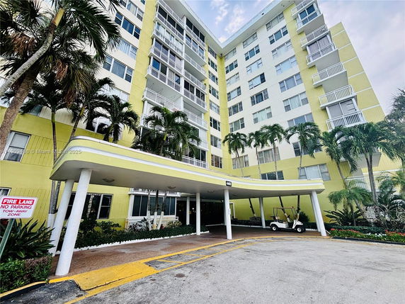 Front view of a multi-story residential building with a covered entrance and palm trees.