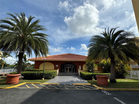 Front view of a building with a red tiled roof and entrance steps, surrounded by palm trees.