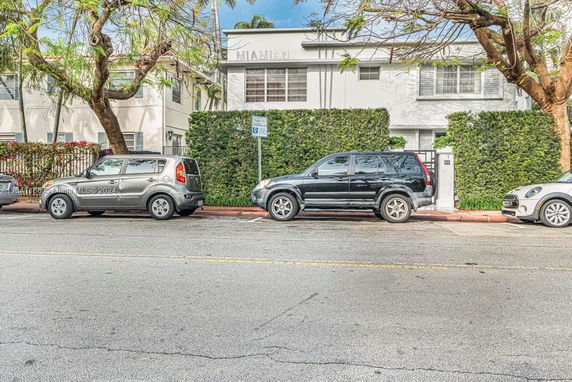 Front view of a two-story building with trees and parked cars in front.