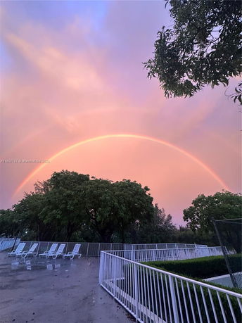 Outdoor view with a rainbow in the sky and lounge chairs by a fence.