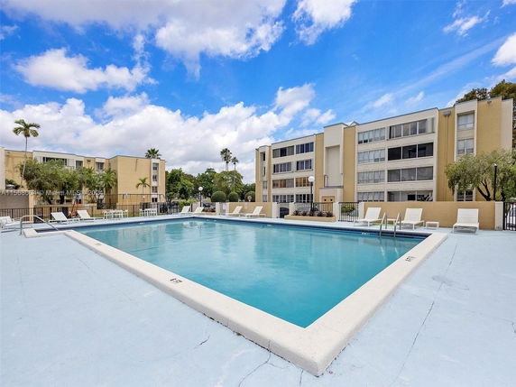 An outdoor swimming pool surrounded by lounge chairs and a multi-story residential building in the background.