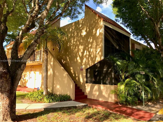 Front view of a two-story building with a screened balcony and staircase.