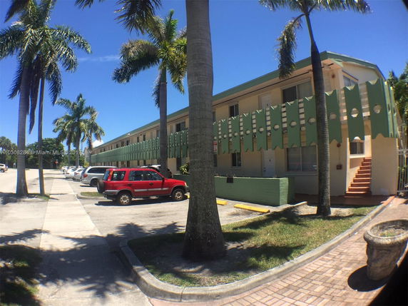 Front view of a two-story residential building with green facade elements and palm trees surrounding it.