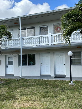 Front view of a two-story building with multiple doors and windows, featuring a balcony and a small lawn area.