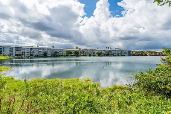Buildings seen from across a body of water with grassy foreground under a cloudy sky.