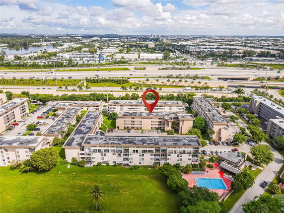 Aerial view of a residential complex with multiple apartment buildings, a swimming pool, and nearby roads.