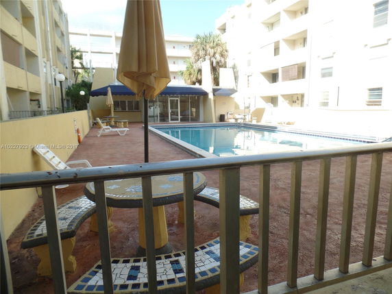 Outdoor pool area of a building complex with lounge chairs and a table set near the pool.