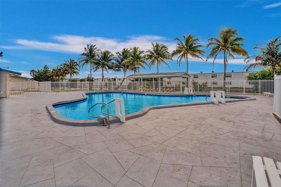 Outdoor swimming pool with surrounding palm trees and a fence.