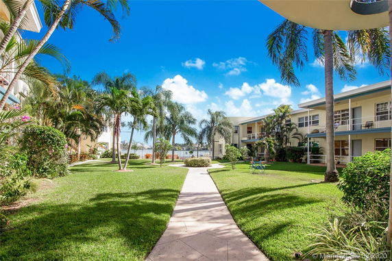 Outdoor area surrounded by two-story residential buildings with balconies, palm trees, and a pathway.