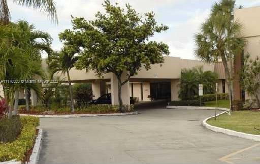 Front view of a building with a driveway and surrounding greenery.