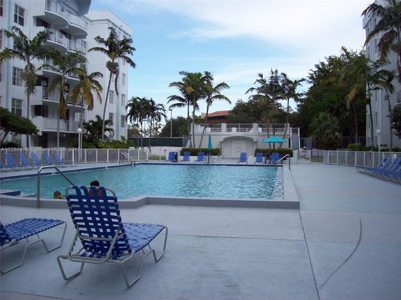 Outdoor swimming pool area with surrounding lounge chairs and nearby buildings.