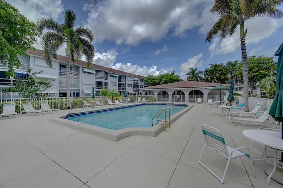 Outdoor swimming pool with surrounding lounge chairs and a building in the background.