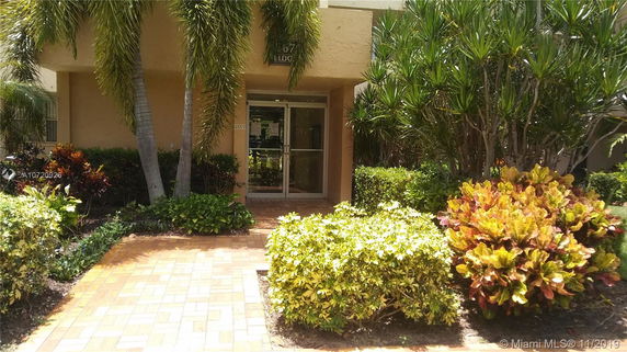 Front view of a building entrance with glass doors, surrounded by tropical plants.