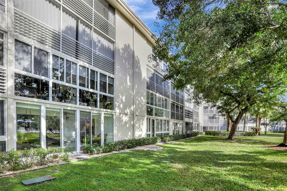 Side view of a multi-story building with large windows and greenery in the foreground.