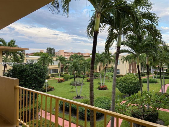 View from a building balcony showing surrounding landscaped garden with palm trees and paths.