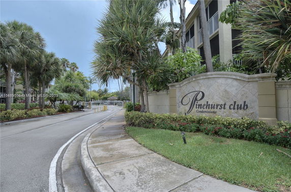 Entrance and front view of Pinehurst Club condominium with a decorative sign and gated driveway.
