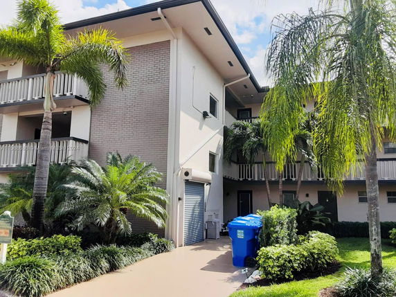 Front view of a multi-story residential building with balconies and palm trees in the foreground.