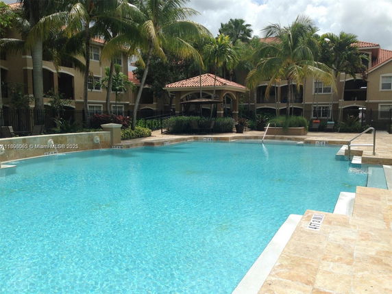 Outdoor swimming pool in front of a multi-story residential building with palm trees.