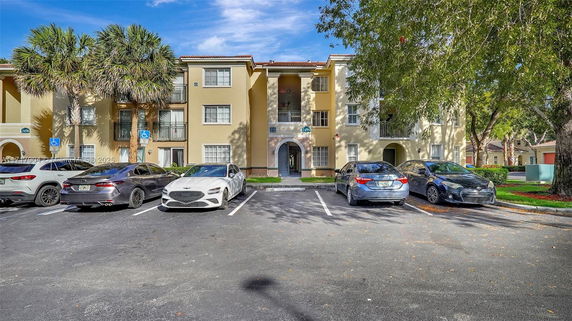 Outdoor parking area with multiple cars in front of a residential building.
