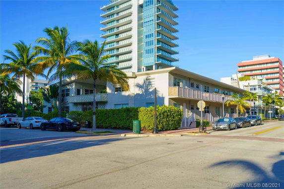 Front view of a multi-story building with balconies and adjacent tall apartment towers.